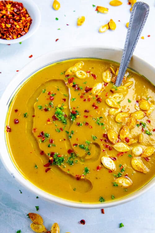 A bowl filled with spicy, silky, creamy pumpkin soup, topped with roasted pumpkin seeds and chili flakes