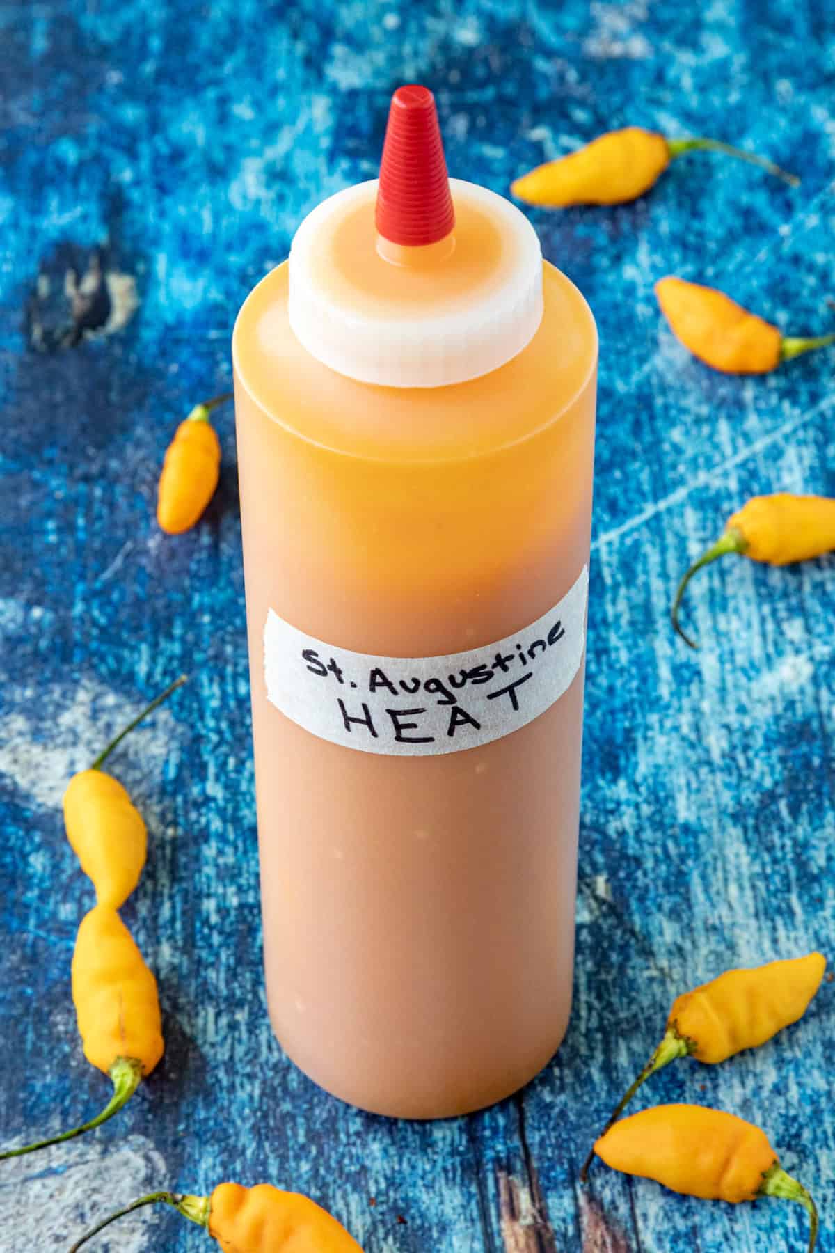A bottle of Mike's St. Augustine Heat Hot Sauce on a table, surrounded by fresh datil chilies