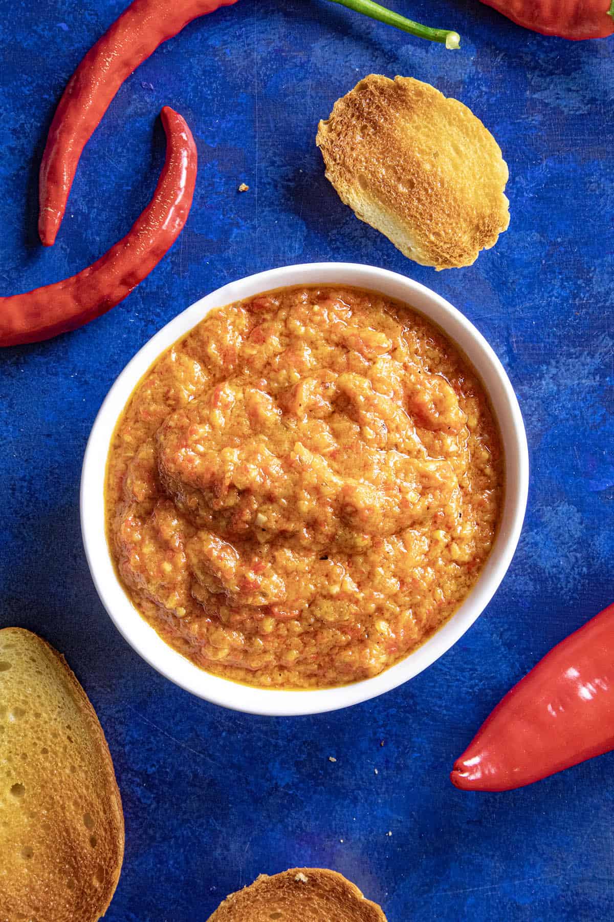 Serbian Roasted Red Pepper Relish (Ajvar) in a bowl, surrounded by crostinis and fresh chilies