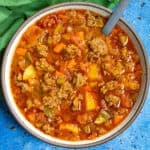 A bowl of chunky hamburger soup with a spoon