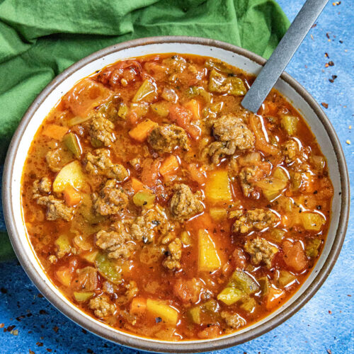 Chunky hamburger soup served in a bowl with a spoon, loaded with potatoes and seasoned ground beef