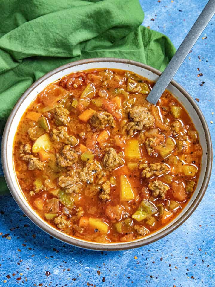 Chunky hamburger soup served in a bowl with a spoon, loaded with potatoes and seasoned ground beef