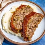 Two thick slices of southern meatloaf on a plate, glazed with tangy tomato sauce, served over creamy mashed potatoes