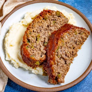 Two thick slices of southern meatloaf on a plate, glazed with tangy tomato sauce, served over creamy mashed potatoes