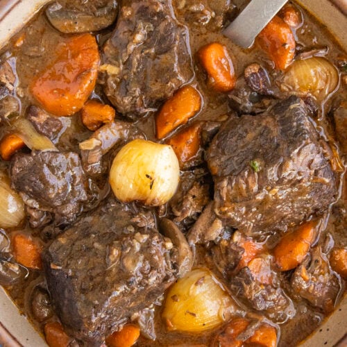 A bowl filled with chunky Beef Bourguignon, with lots of pearl onion, carrots, and meat