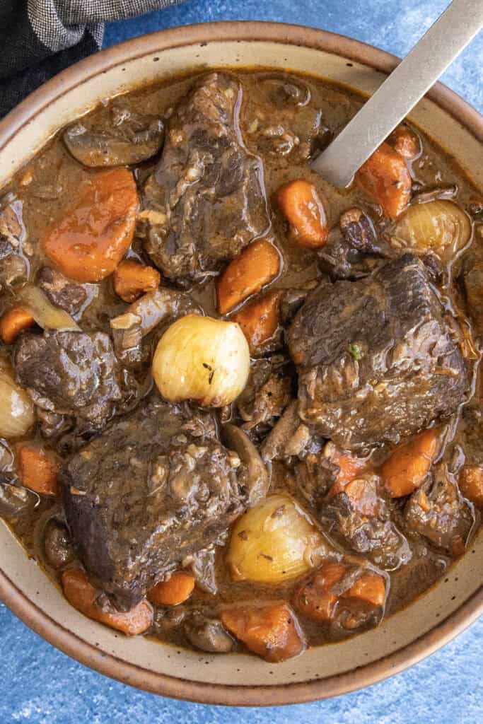 A bowl filled with chunky Beef Bourguignon, with lots of pearl onion, carrots, and meat