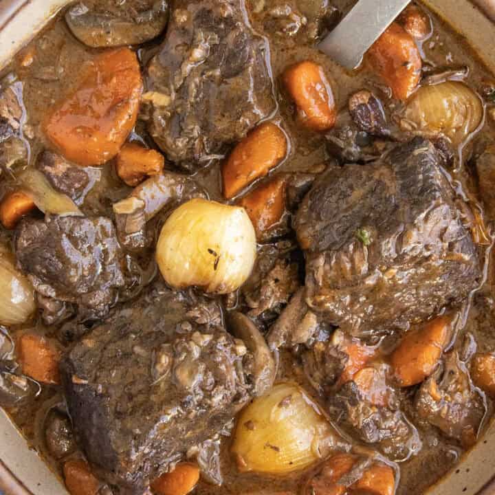 A bowl filled with chunky Beef Bourguignon, with lots of pearl onion, carrots, and meat