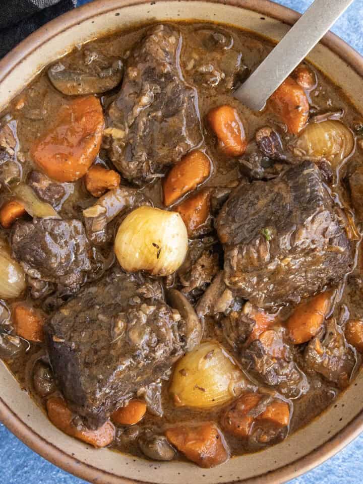 A bowl filled with chunky Beef Bourguignon, with lots of pearl onion, carrots, and meat