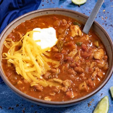 Homemade Chicken Chili in a bowl, topped with shredded cheddar cheese and sour cream