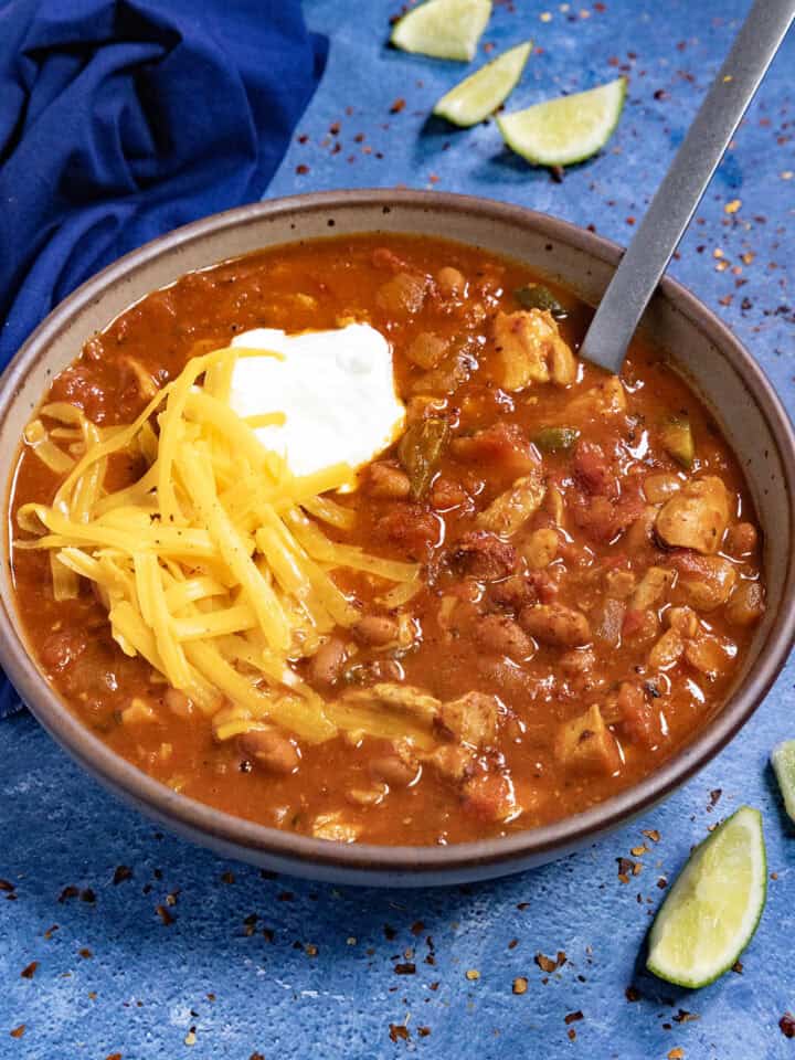 Homemade Chicken Chili in a bowl, topped with shredded cheddar cheese and sour cream
