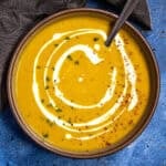 Curried Butternut Squash Soup served in a bowl, garnished with a cream swirl, fresh cilantro, and chili flakes