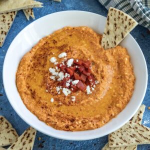 A bowl of Greek Whipped Feta Dip with Roasted Red Peppers (Htipiti) garnished with chopped peppers and feta