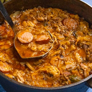 A scoop of Bigos (Polish Hunter's Stew) being served from the simmering pot