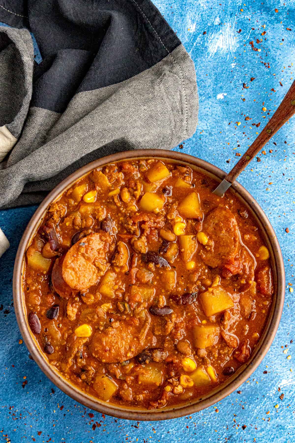 Cowboy stew in a serving bowl with lots of potatoes, smoked sausage, beans, corn, and more.