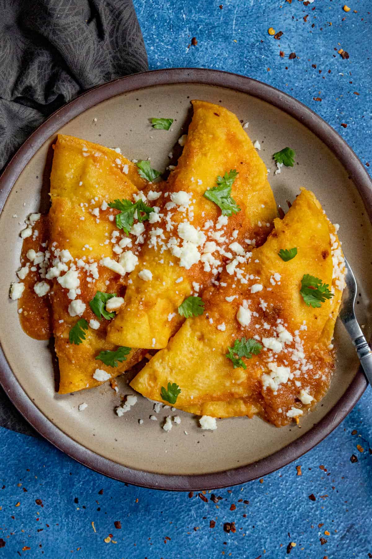 Three folded fried and stuffed tortillas (Entomatadas) on a plate, topped with tomato sauce and queso fresco
