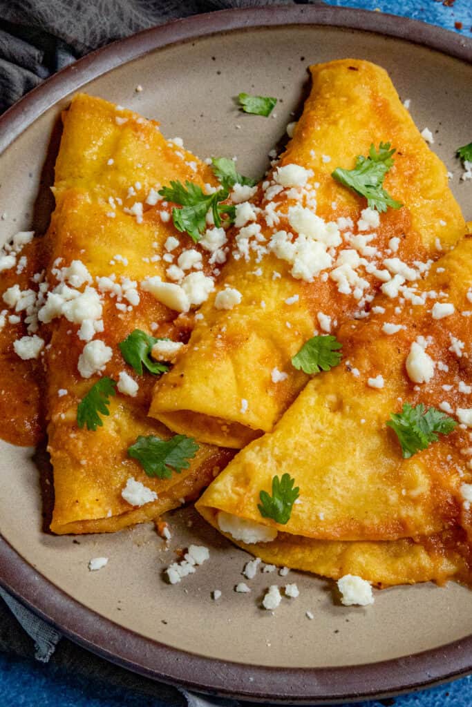 3 lightly fried corn tortillas, stuffed with cheese, aka entomatadas, served on a plate then topped with tomato sauce and crumbly cheese