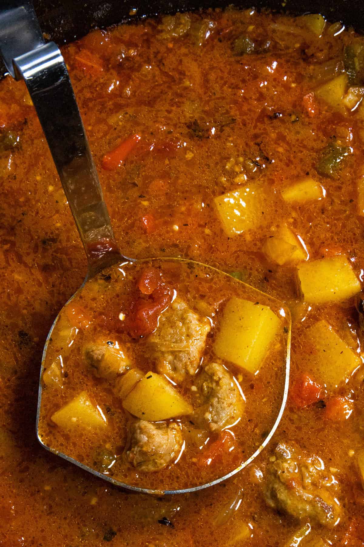 A large scoop of Italian Sausage and Potato Soup, loaded up with chunky potatoes and sausage, ready to be served into a bowl