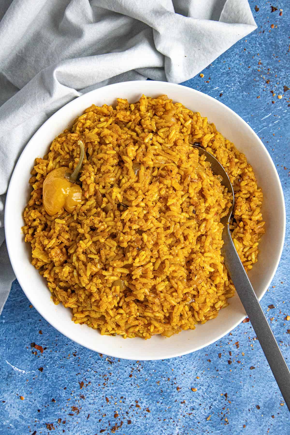 A white bowl filled with fluffy and spicy jollof rice, with a Scotch bonnet chili on top