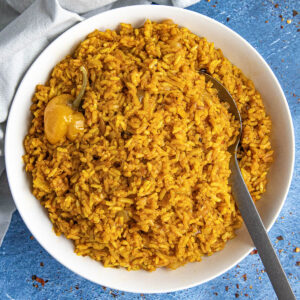 Spicy jollof rice in a white bowl with a serving spoon