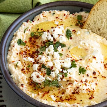 Greek Spicy Feta Dip (Tirokafteri) in a bowl, topped with fresh chopped parsley, red chili flakes, and crumbly feta cheese