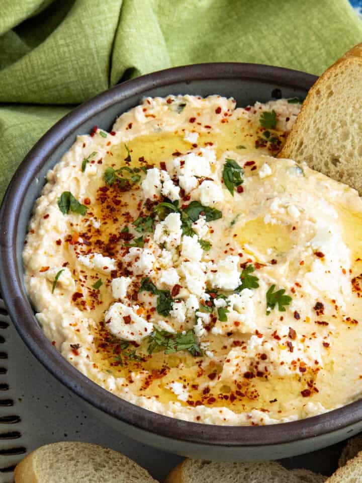Greek Spicy Feta Dip (Tirokafteri) in a bowl, topped with fresh chopped parsley, red chili flakes, and crumbly feta cheese