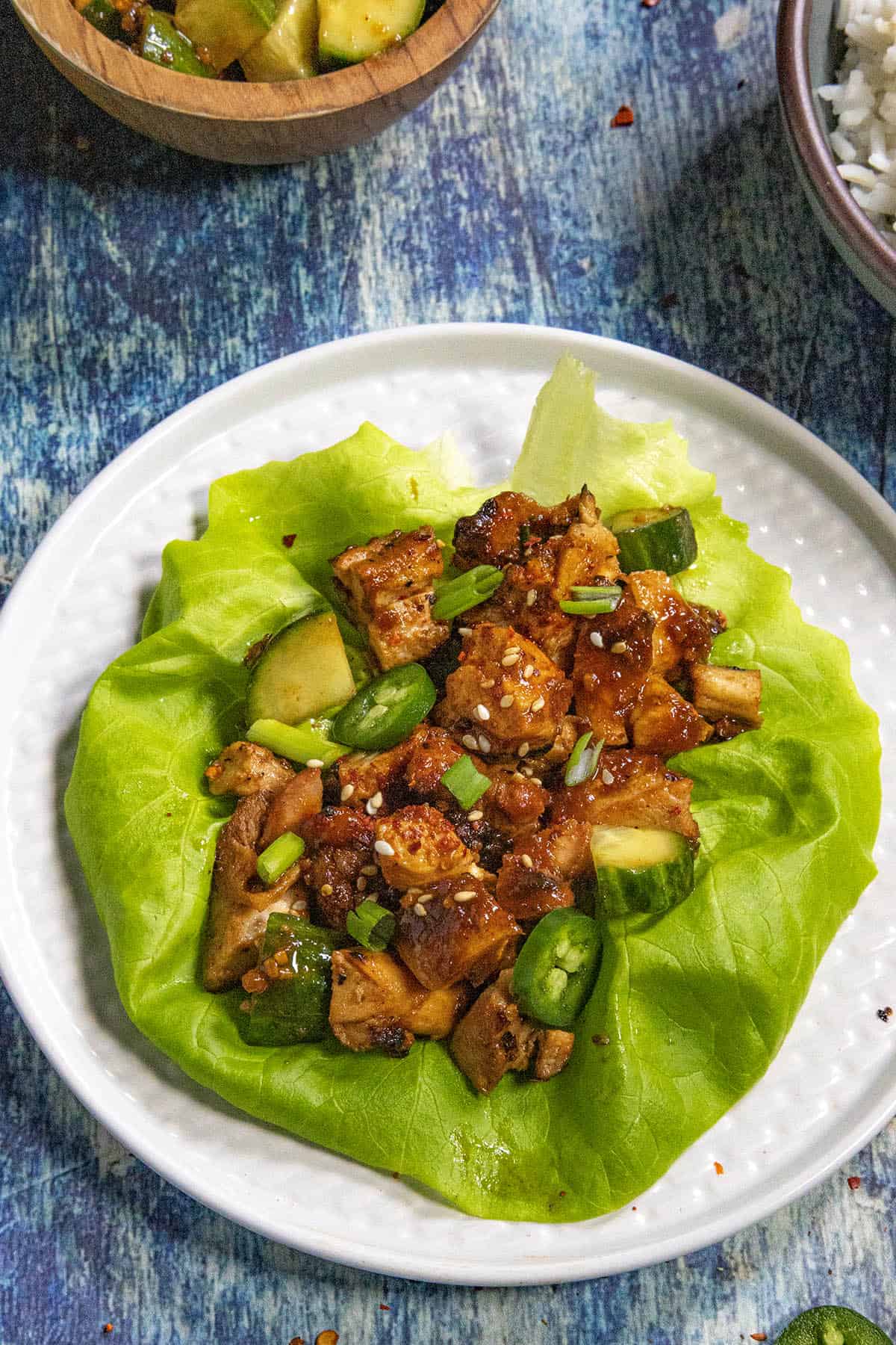 Chopped Korean BBQ Chicken (dak bulgogi) piled onto a lettuce wrap, garnished with sliced chilies and cucumber kimchi