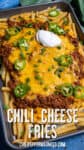 A tray of chili cheese fries piled high with melted cheese, hearty ground chili, fresh jalapeños, green onions, and a dollop of sour cream.