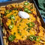 A baking dish loaded with hearty chili cheese fries, topped with sour cream