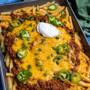 A baking dish loaded with hearty chili cheese fries, topped with sour cream