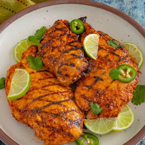 3 chili lime chicken breasts with char grill marks on a plate, garnished with lime, cilantro, and sliced jalapeno