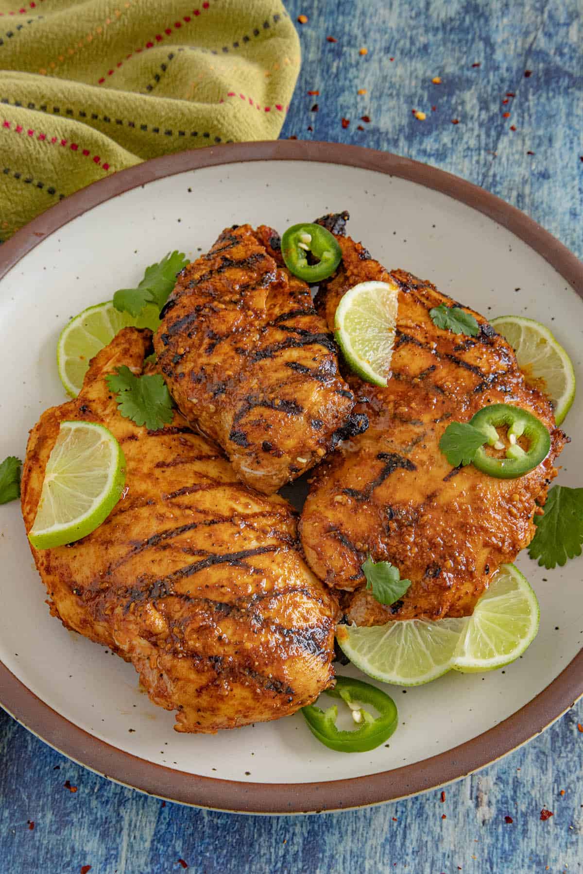 3 chili lime chicken breasts with char grill marks on a plate, garnished with lime, cilantro, and sliced jalapeno