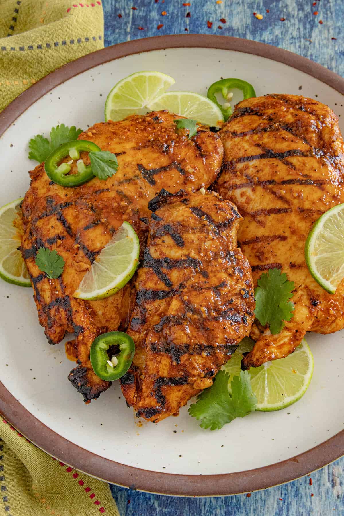 3 pieces of chili lime chicken served on a white place with lime garnish, fresh cilantro, and sliced chilies