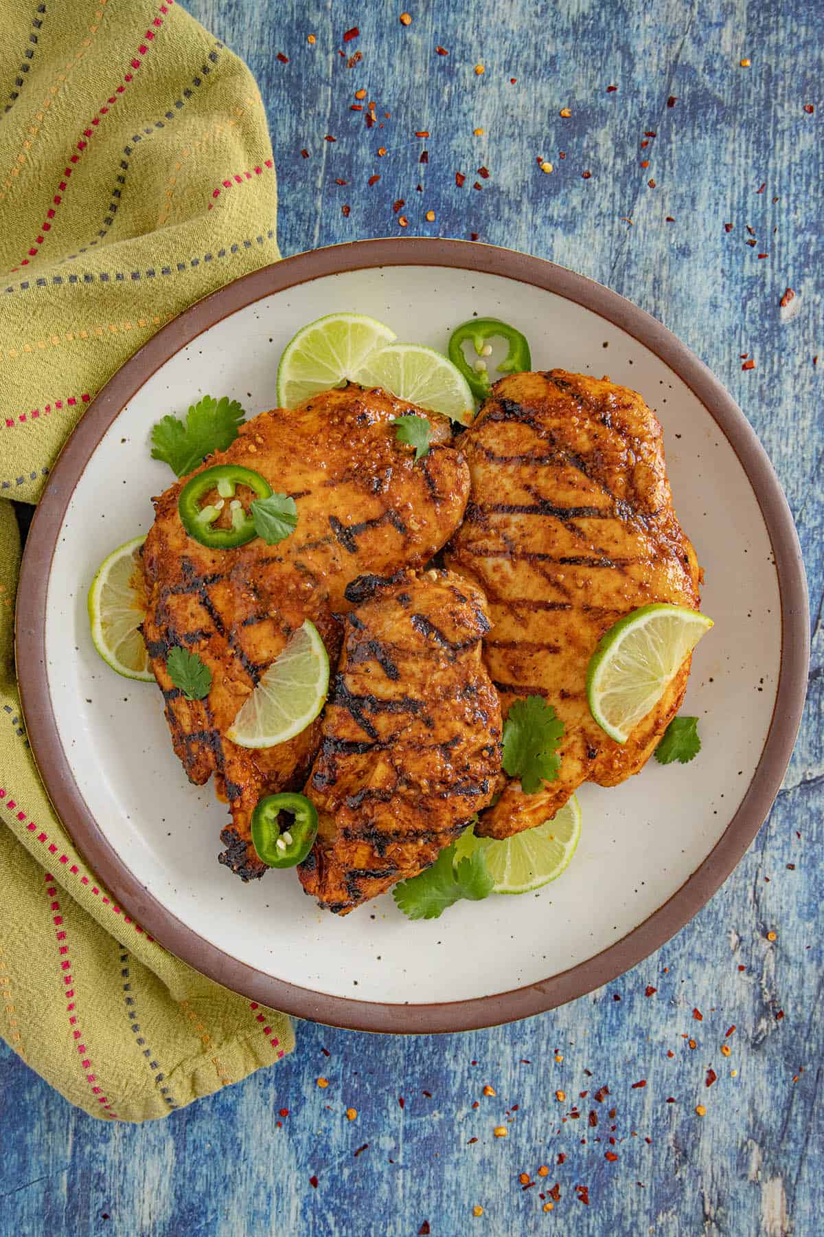 3 grilled chicken breasts with chili lime sauce on a serving plate with lime and cilantro garnish