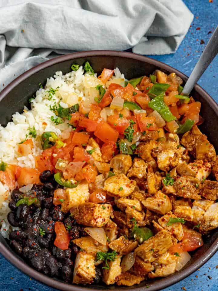 A bowl of chopped chipotle chicken served with white rice and black beans, topped with chunky salsa