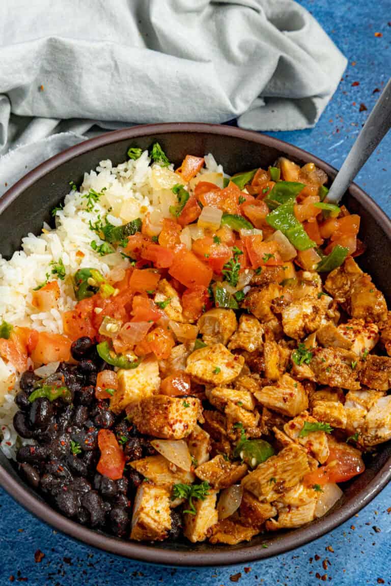 A bowl of chopped chipotle chicken served with white rice and black beans, topped with chunky salsa
