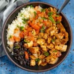 A bowl filled with chopped chipotle chicken served with white rice, black beans, and topped with fresh salsa