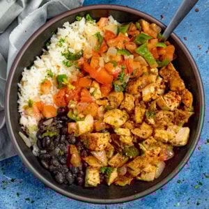 A bowl filled with chopped chipotle chicken served with white rice, black beans, and topped with fresh salsa