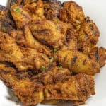 A dozen crispy grilled chicken wings on a plate, dripping with cowboy butter