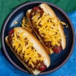 Two chili dogs loaded up with shredded cheddar and thick hot dog chili