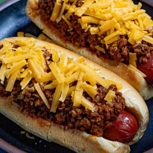 Two chili dogs topped with thick, meaty hot dog chili and shredded cheddar cheese