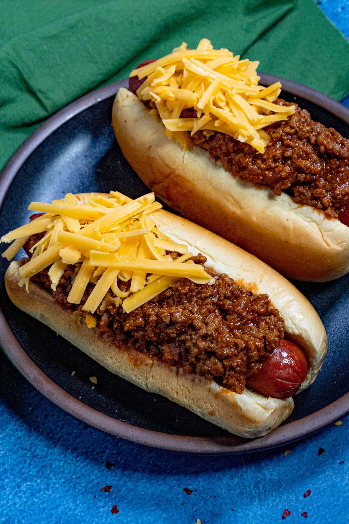 Two chili dogs topped with lots of hot dog chili and shredded cheddar