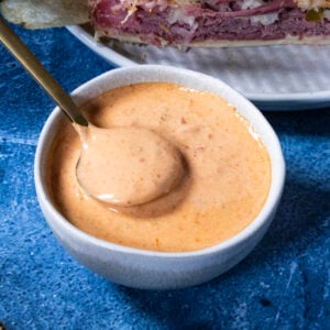 Creamy Russian dressing in a bowl with a spoon, served with homemade Reuben sandwiches