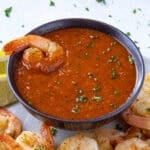 A piece of spicy shrimp dipped into a bowl of zingy homemade cocktail sauce