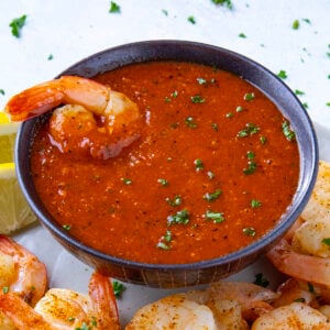A piece of spicy shrimp dipped into a bowl of zingy homemade cocktail sauce