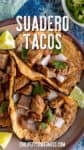 Three Suadero Tacos filled with chopped beef, onions, and cilantro are served on a plate with lime wedges.