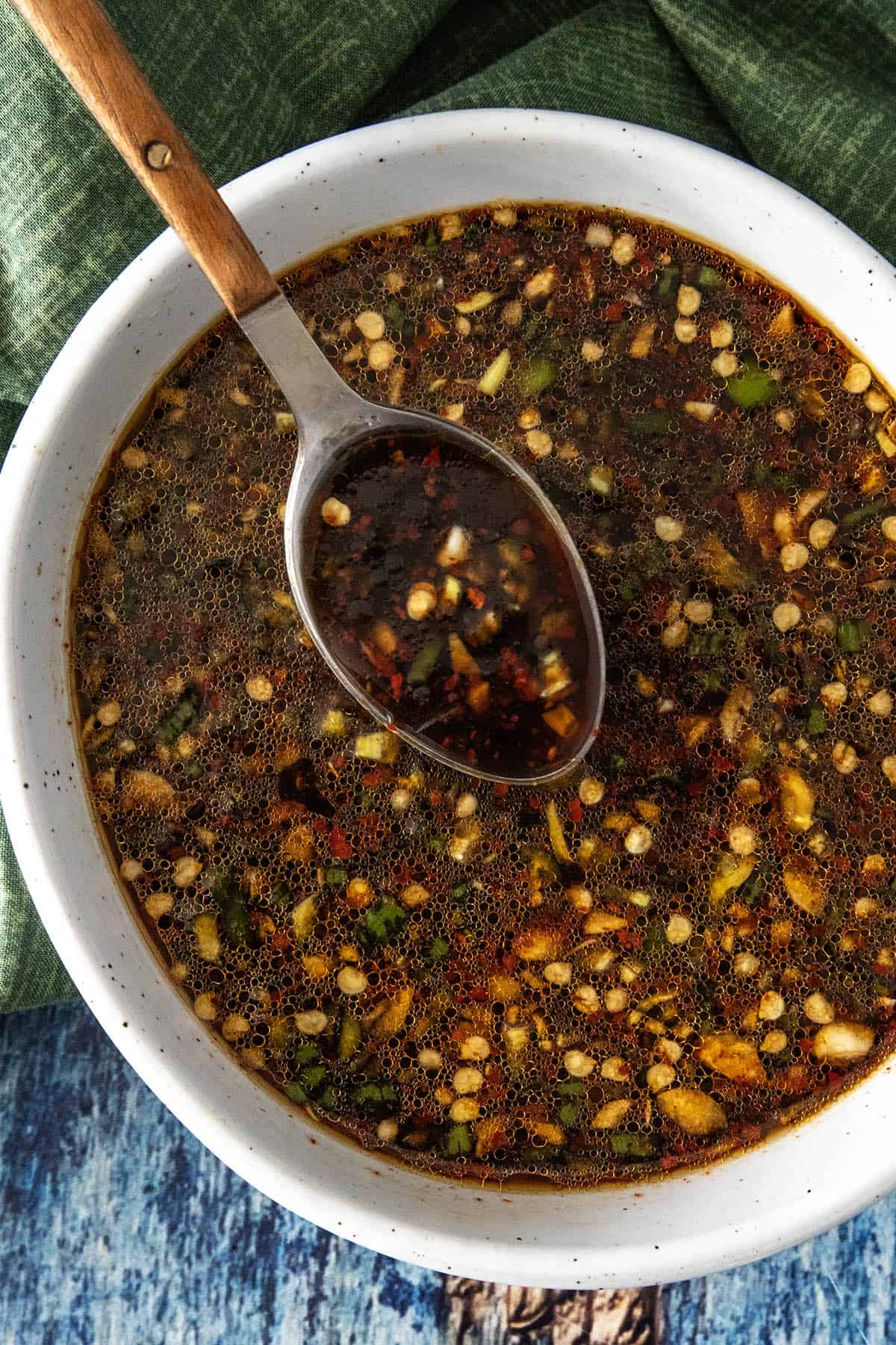 A close-up view of a bowl filled with the best Teriyaki Marinade, containing chopped green onions, garlic, chili flakes, and sesame seeds, with a spoon lifting some sauce from the bowl.