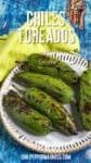 A plate of Chiles Toreados—roasted green chiles—sits on a white scalloped dish atop a blue wooden table with a yellow napkin. Text reads Chiles Toreados and chilipeppermadness.com.