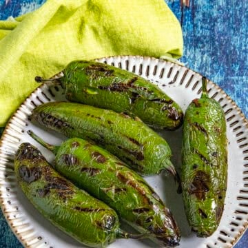 Chiles toreados recipe with five charred blistered jalapenos on a plate, drizzled with lime, on a blue wooden surface.