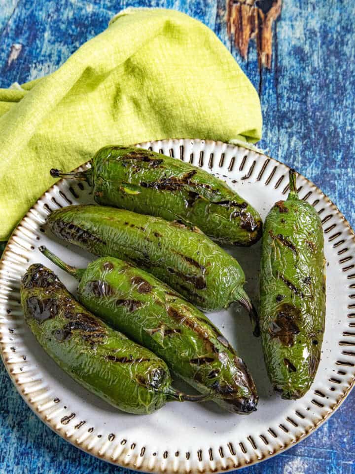 Chiles toreados recipe with five charred blistered jalapenos on a plate, drizzled with lime, on a blue wooden surface.