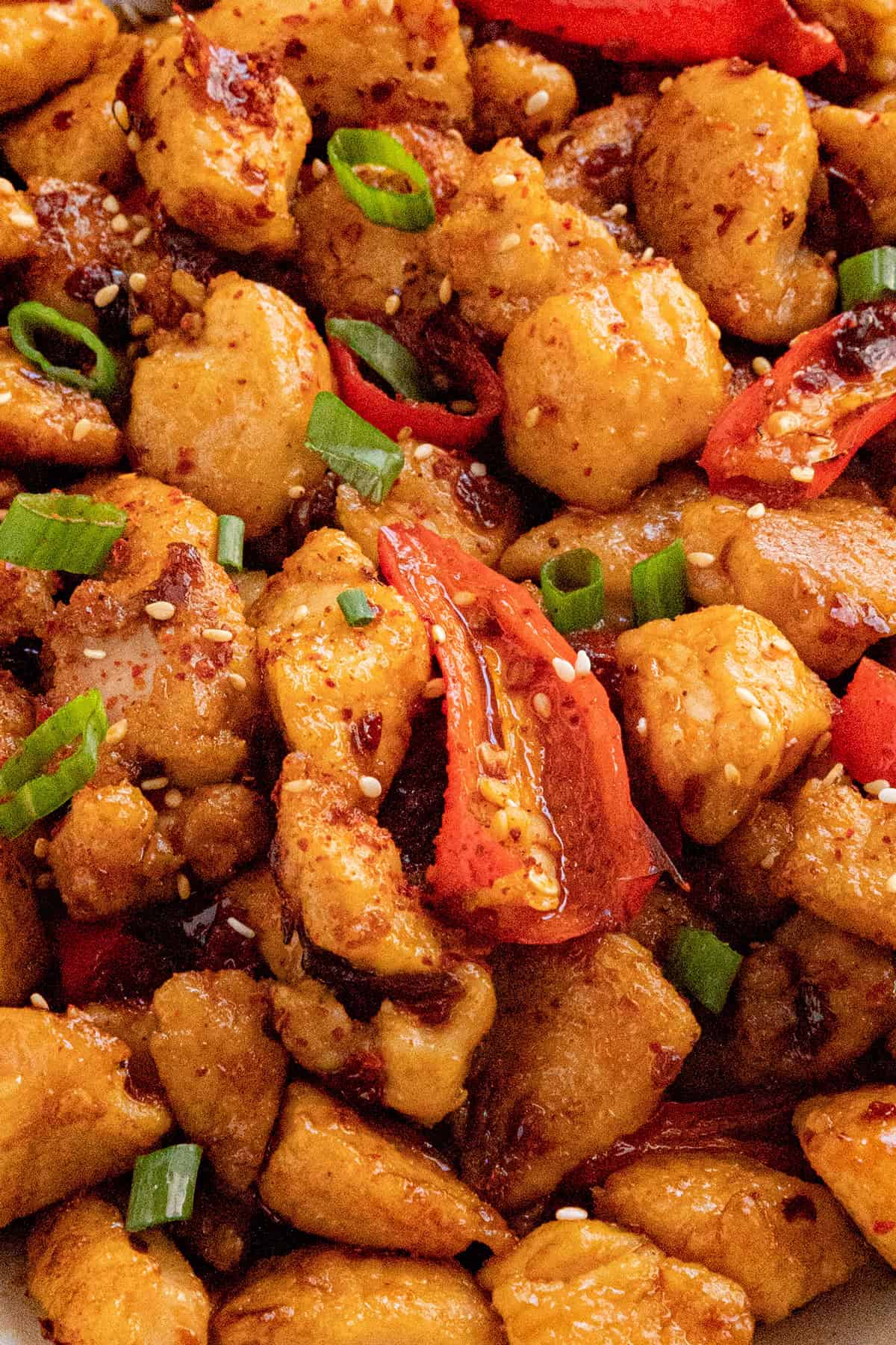 Close-up of crispy chili crisp chicken with red bell peppers, garnished with chopped green onions and sesame seeds. The dish appears flavorful and well-seasoned.